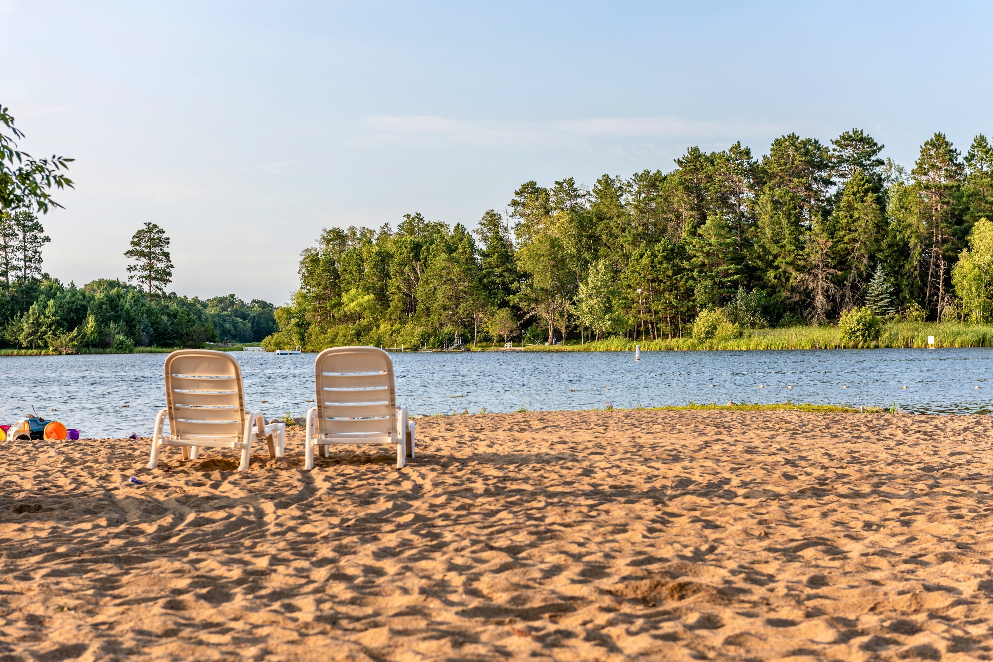 two lounge chairs on gold sand with lake water and trees in background